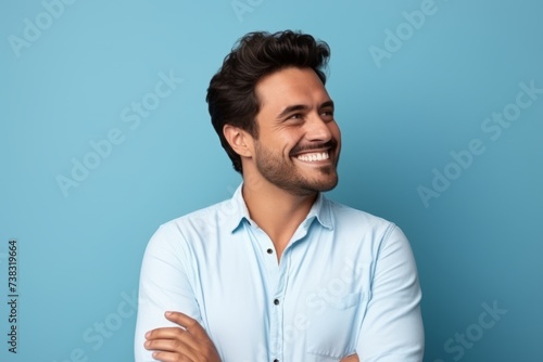 Portrait of a handsome young man smiling and looking away against blue background © Igor