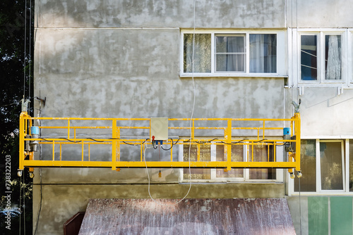 High-altitude works, residential building facade plastering. Suspended motor scaffolding platform on facade of residential building under renovation