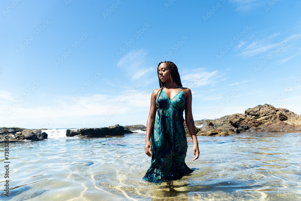 Beautiful woman with braids and blue dress in the beach water walking towards the camera Beautiful woman with braids and blue dress in the beach water walking towards the camera