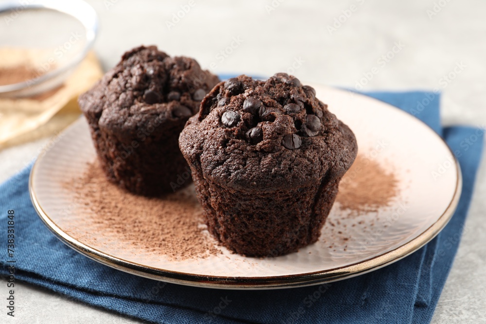 Delicious chocolate muffins and cacao powder on light grey table, closeup Delicious chocolate muffins and cacao powder on light grey table, closeup
