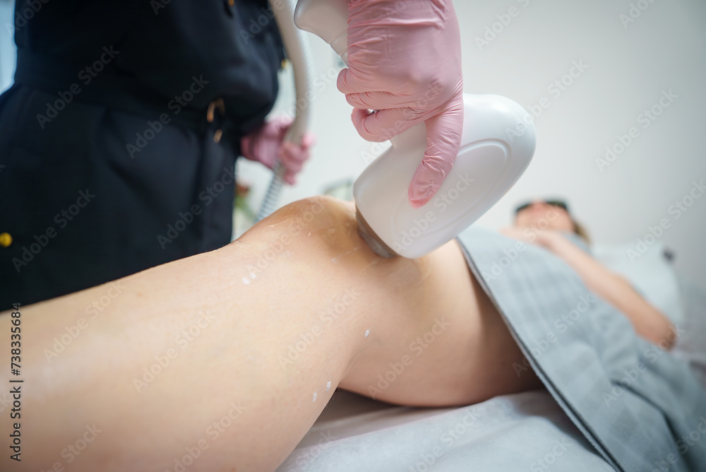Naklejka premium Closeup of a laser hair removal or skin rejuvenation treatment on a client's leg by a gloved professional in a clean salon environment, with a focus on the action and care.