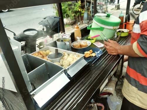 The seller preparing siomay to serve the customer. PKL or MSME concept. Siomay is Indonesian street food, consist of dumpling, steamed potato, egg and tofu with peanut sauce photo