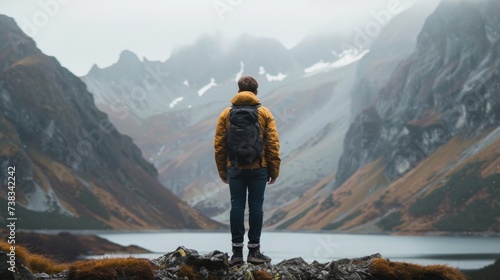 Amidst the fog and snow, a lone hiker stands on rocky terrain, gazing at the majestic mountain range before him, his outdoor clothing blending seamlessly with the rugged landscape photo