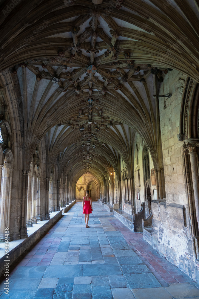 Lady in red dress is walking along a beautiful cloister at Canterbury Cathedral