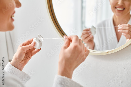 cropped view of adult woman in cozy bathrobe cleaning her teeth with dental floss in bathroom photo
