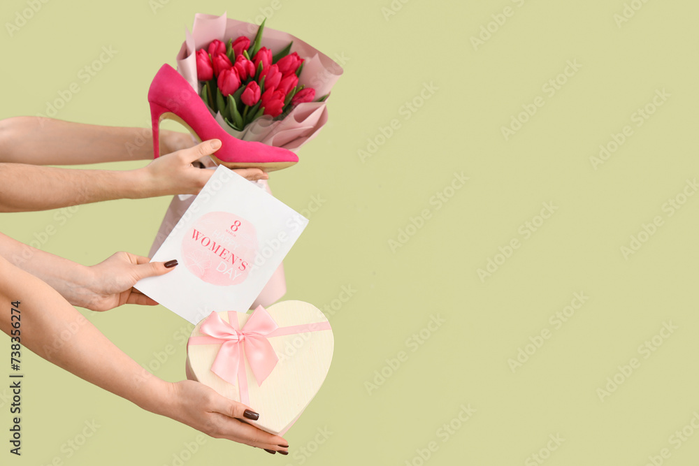 Female hands with bouquet of tulips, gift box and festive postcard on green background. Shopping for International Women's Day