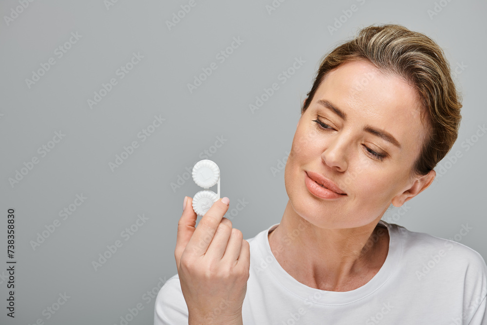 good looking jolly woman with blonde hair holding contact lenses and looking away on gray backdrop good looking jolly woman with blonde hair holding contact lenses and looking away on gray backdrop
