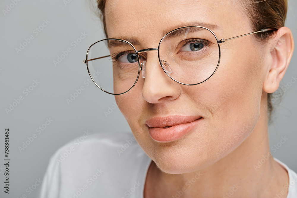joyful beautiful woman with blonde collected hair and glasses smiling at camera on gray backdrop joyful beautiful woman with blonde collected hair and glasses smiling at camera on gray backdrop