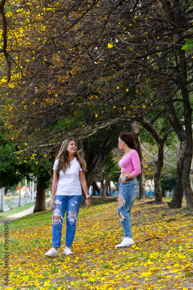 Obraz premium two adult female friends talking and walking in field full of yellow flowers during summer