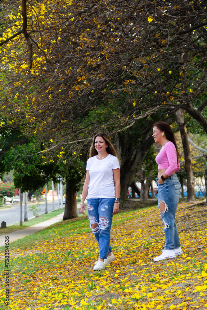 Obraz premium two adult female friends talking and walking in field full of yellow flowers during summer