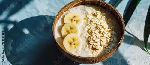 Top view of a healthy summer breakfast: Collagen powder, smoothie with banana, pineapple, and gluten-free oats in a coconut shell bowl with strong shadows.
