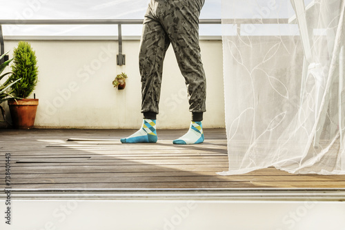 Legs of a man wearing elastic pants with a mimetic print walking on a terrace with a wooden floor photo