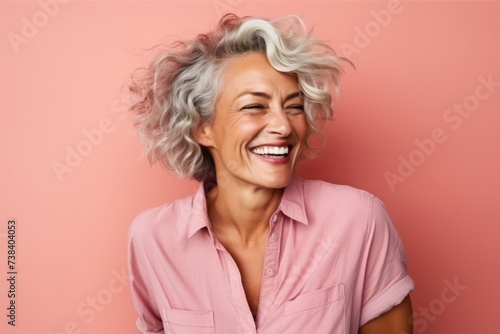 Portrait of a happy senior woman laughing against a pink background.