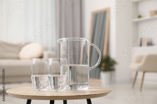 Jug and glasses with clear water on wooden table indoors. Space for text