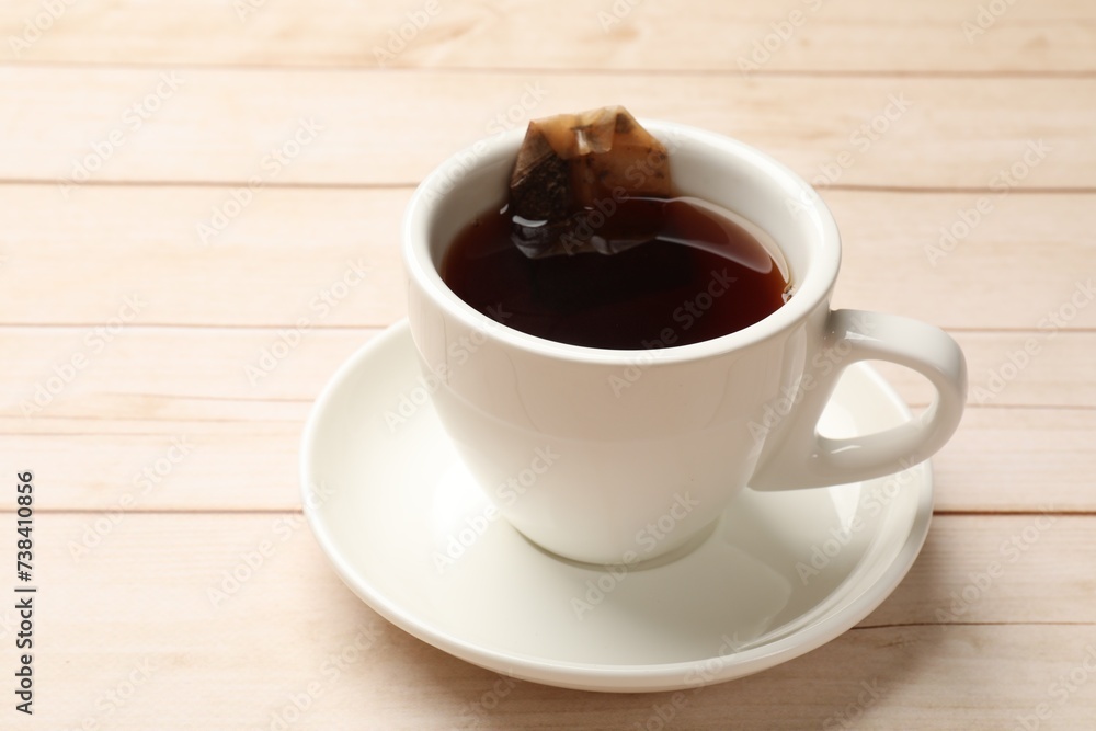 Obraz premium Tea bag and cup of hot beverage on light wooden table, closeup