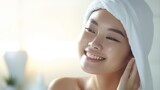 A Closeup head shot of a young beautiful Asian woman applying facial moisturizer after bathing. Smiling beautiful woman wrapped in towel to smooth her skin Daily routine in the morning.