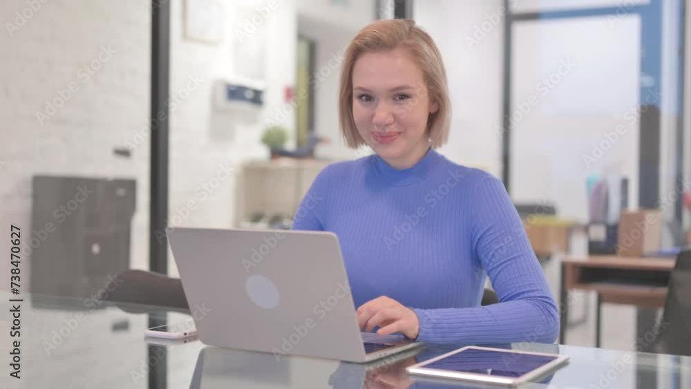 Young Woman Smiling at Camera while Working on Laptop in Office Young Woman Smiling at Camera while Working on Laptop in Office