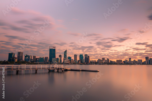 Jetty at South Perth foreshore  Western Australia overlooking city skyline. Water reflections on swan river with cloudy sky  pink  purple  blue hues mirrored on still water  buildings  city  dawn