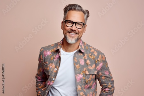 Handsome mature man in eyeglasses smiling at camera while standing against pink background