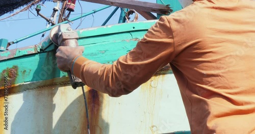 Close up of a worker buffing the hull of a wooden fishing vessel with the electric sander at a boatyard photo