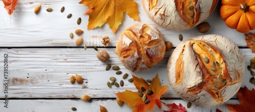 Top view of a white wooden background with home-baked fresh bread adorned by autumn decor like pumpkin seeds, fall leaves, and a concept of pumpkin and the changing season. The lighting casting hard