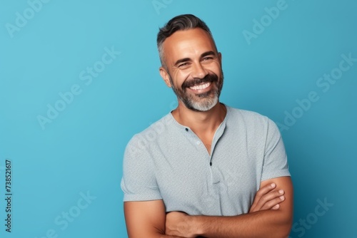 Portrait of handsome mature man in casual t-shirt, looking at camera and smiling, standing against blue background