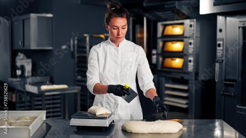 A female baker in uniform weighs evenly shaped dough on kitchen surface before baking in the oven photo