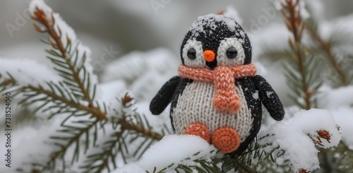 Knitted penguin toy in the snow against a background of fir branches. The concept of winter and holidays.