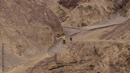 Unidentifiable distant hikers with backs to camera enjoying the mild temperatures winter affords while walking a trail at Artist Point in Death Valley National Park, California, USA
