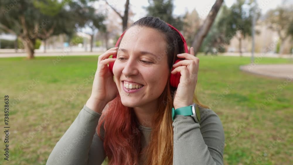 A cheerful woman adjusts red headphones in a park A cheerful woman adjusts red headphones in a park