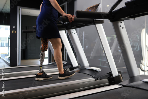 Athletic woman with a disability walking on a treadmill while exercising in a gym.