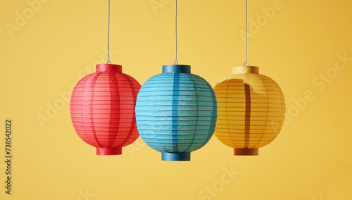Three colorful paper lanterns on a yellow background, reflecting Japanese-inspired imagery, industrial and product design, innovating techniques, and mundane materials in dark teal and light red hues.