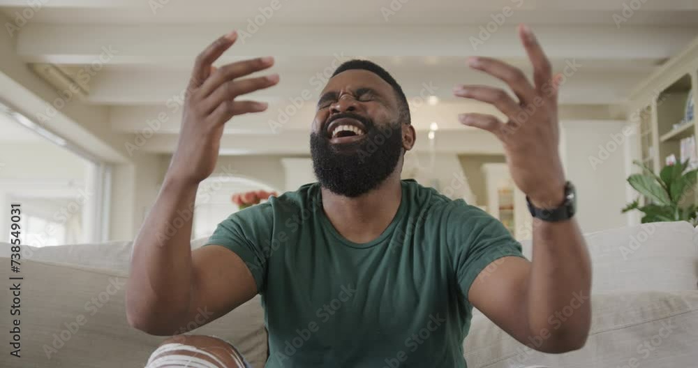 An African American man laughs on a couch in a cozy room on a video call An African American man laughs on a couch in a cozy room on a video call