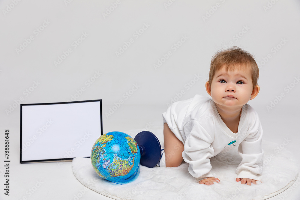 Earth day concept. Portrait of a infant baby girl in a white bodysuit with inscription my world sitting with the earth globe and empty white board on white background. Save the planet. Mock up Earth day concept. Portrait of a infant baby girl in a white bodysuit with inscription my world sitting with the earth globe and empty white board on white background. Save the planet. Mock up