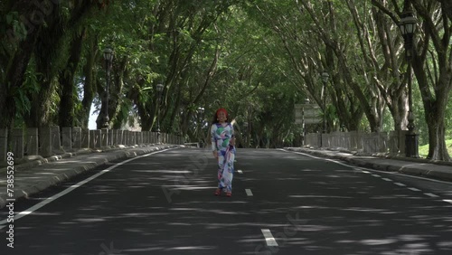 Wallpaper Mural Asian woman in a colored stylish dress with turban walks and dance along the asphalt road under shady trees in the park. Portrait of a woman in motion between trees. Torontodigital.ca