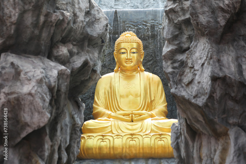 The big golden Buddha statue with waterfall and stone wall in background at Wat Lak Si Rat Samoson, Samut Sakhon, Thailand. photo