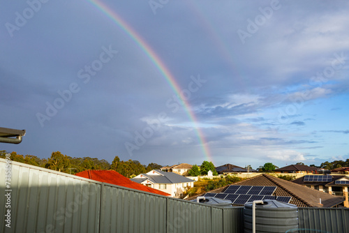 Rainbow over suburban rooftops in residential area with sunlight on damp solar panels after rain photo