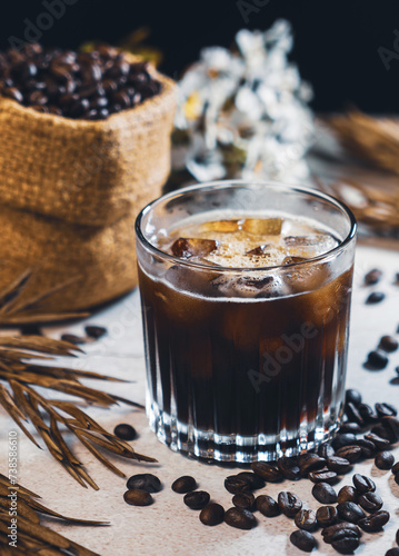 Ice coffee black in a glass and coffee beans. Cold summer drink on wooden table with copy space. Iced americano coffee.