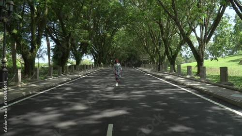 Wallpaper Mural Asian woman in a colored stylish dress with turban walks and dance along the asphalt road under shady trees in the park. Portrait of a woman in motion between trees Torontodigital.ca