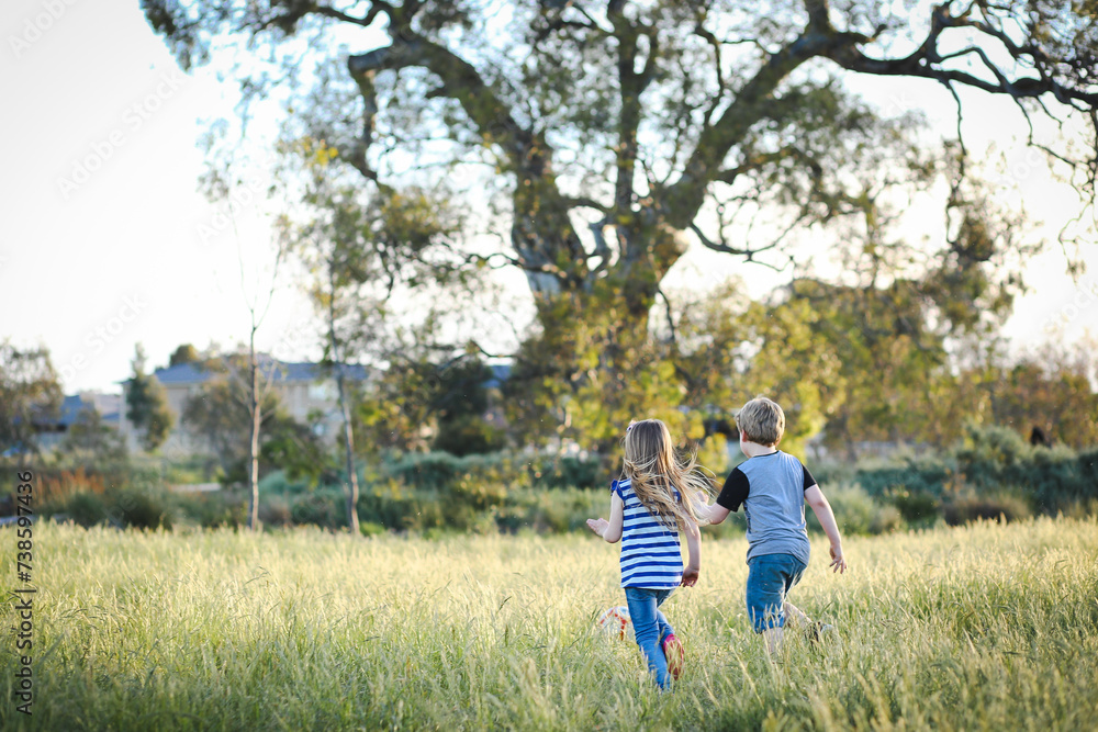Boy and girl running through long grass playing soccer at the park. Aussie kids having fun outdoors Boy and girl running through long grass playing soccer at the park. Aussie kids having fun outdoors