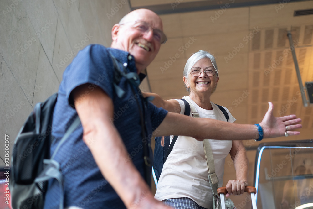 Obraz premium Smiling senior couple in airport departure area on escalators going towards boarding. Travel and tourism concept, people with luggage