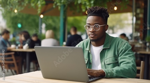 A young black African man with glasses is working on his laptop.