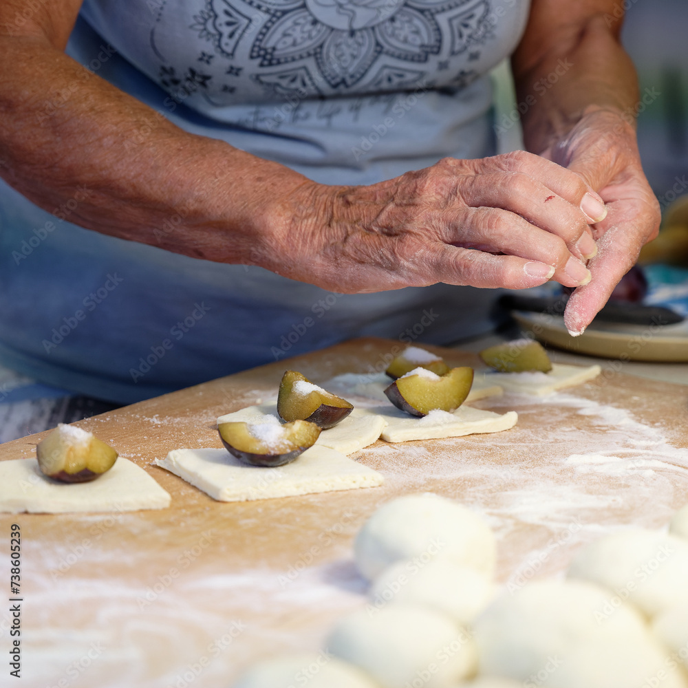 Preparation of homemade fruit dumplings with plums. Czech specialty of sweet good food. Dough on kitchen wooden table with hands.