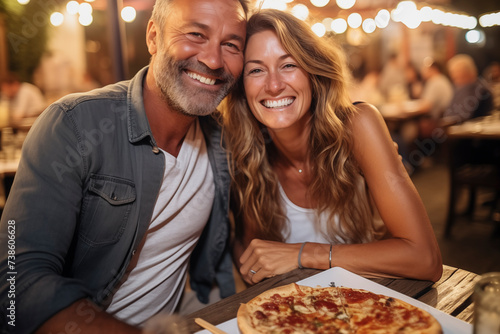 Happy adult cute couple have fun eating a pizza together outdoor in traditional italian pizzeria restaurant sitting and talking and laughing. People enjoying food and travel lifestyle. Tourism photo
