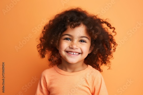 Portrait of a smiling little girl with curly hair over orange background © Loli