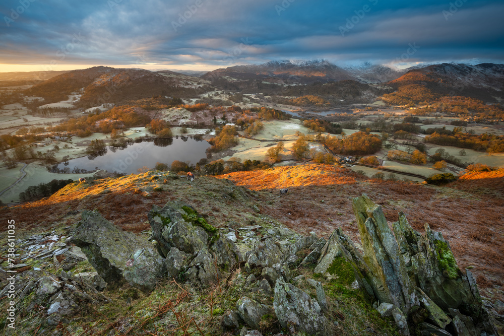Wide angle view of Loughrigg Tarn at sunrise with golden light on a frosty landscape. Lake District, UK.