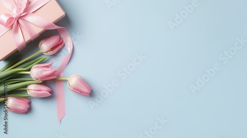 Mother's Day decorations concept. Top view photo of blue giftbox with ribbon bow and bouquet of pink tulips on isolated pastel pink background with copyspace