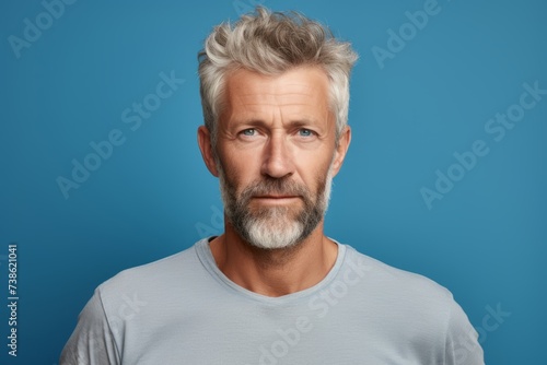 Portrait of mature man with grey hair and beard on blue background