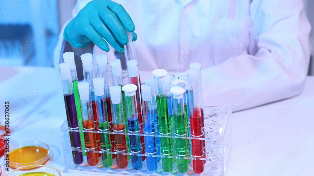 Scientists are doing research in a science lab. A medical chemist in a white coat, gloves and goggles looks at a glass tube. Compare two different liquid samples. and discuss future experiments.