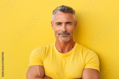 Handsome mature man in yellow t-shirt over yellow background © Loli